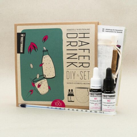 Die Verpackung des Geschenktes steht aufrecht, daraus schaut der Filterbeutel und die Anleitung, daneben stehen zwei Enzymfläschchen, davor liegt das Glasthermometer.